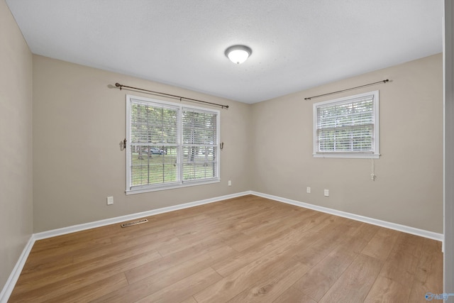 spare room featuring visible vents, light wood finished floors, baseboards, and a healthy amount of sunlight