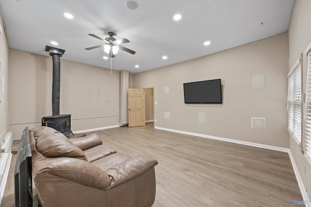 living room with ceiling fan, a wood stove, light wood finished floors, baseboards, and recessed lighting