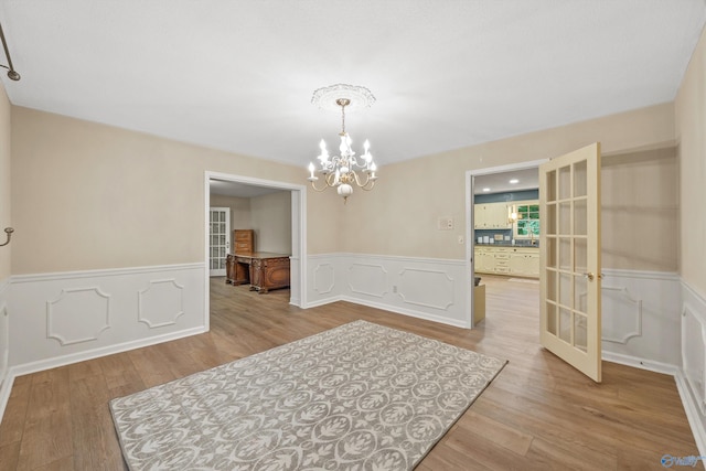 spare room featuring light hardwood / wood-style flooring, french doors, and a notable chandelier