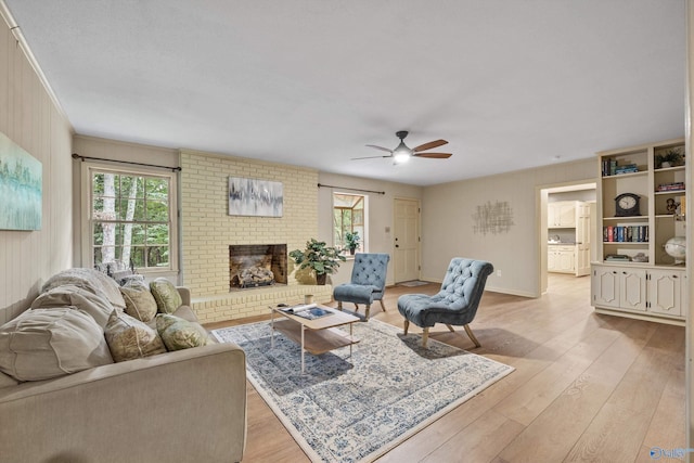 living area with ceiling fan, a wealth of natural light, a fireplace, and light wood-style flooring