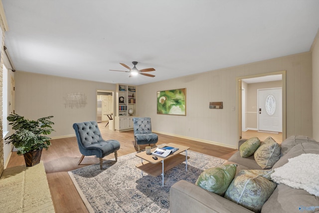 living area featuring ceiling fan, baseboards, wood walls, and light wood finished floors