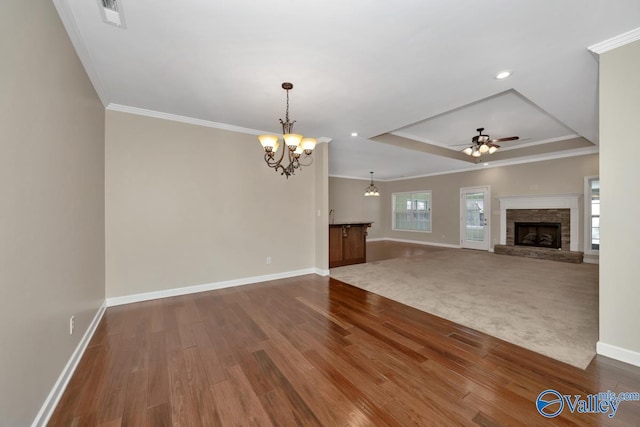 unfurnished living room with ceiling fan with notable chandelier, a raised ceiling, crown molding, a fireplace, and hardwood / wood-style floors