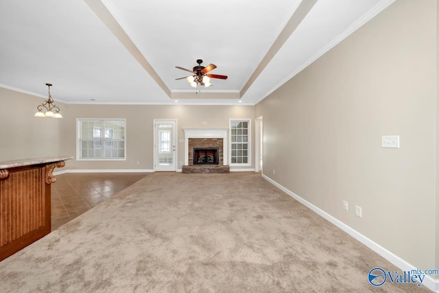 unfurnished living room with a stone fireplace, tile patterned flooring, a tray ceiling, ceiling fan with notable chandelier, and ornamental molding