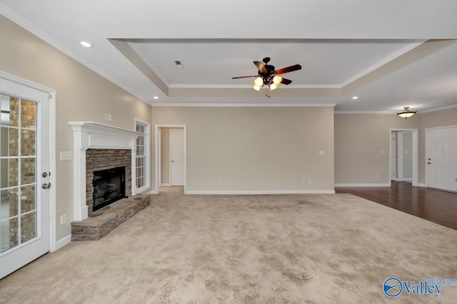 unfurnished living room with a tray ceiling, light carpet, a fireplace, and ornamental molding