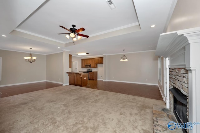 unfurnished living room featuring carpet flooring, a tray ceiling, a stone fireplace, and ornamental molding