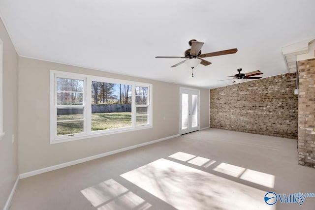 empty room featuring french doors, ceiling fan, a wealth of natural light, and brick wall