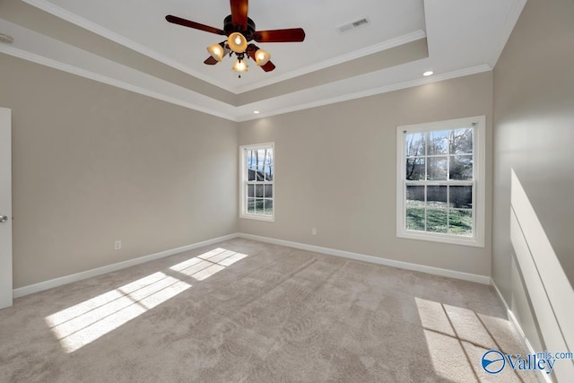 empty room with ceiling fan, light colored carpet, a wealth of natural light, and a tray ceiling