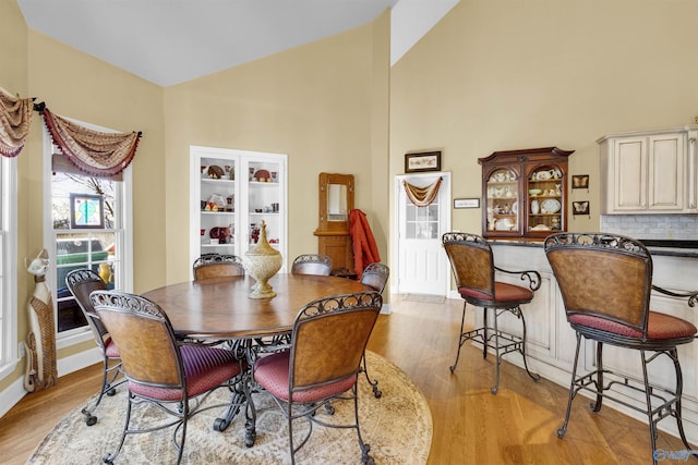 dining room with high vaulted ceiling, light wood-type flooring, and indoor bar