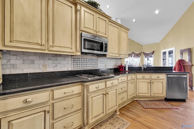 kitchen featuring light wood-type flooring, lofted ceiling, sink, tasteful backsplash, and appliances with stainless steel finishes