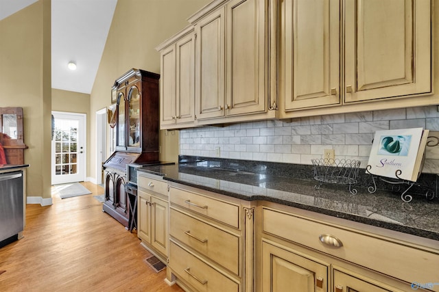 kitchen with light wood-type flooring, backsplash, vaulted ceiling, dishwasher, and dark stone counters