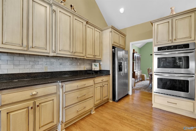 kitchen with dark stone countertops, lofted ceiling, stainless steel appliances, and decorative backsplash