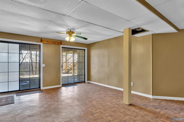 interior space with ceiling fan, a paneled ceiling, parquet floors, and wooden walls