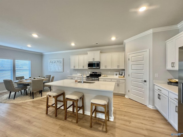 kitchen featuring appliances with stainless steel finishes, a sink, ornamental molding, a kitchen breakfast bar, and white cabinets