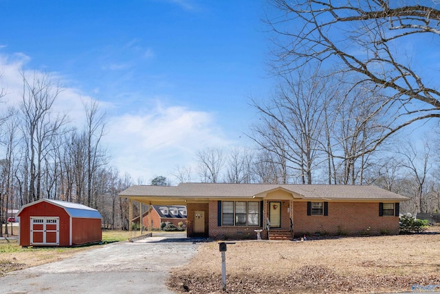 view of front of home featuring an outbuilding, brick siding, driveway, a carport, and a storage unit