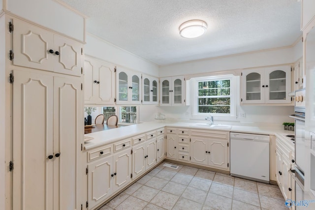 kitchen with white dishwasher, glass insert cabinets, a textured ceiling, and a sink