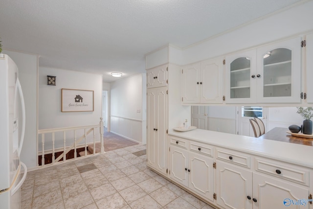 kitchen featuring freestanding refrigerator, light countertops, glass insert cabinets, and white cabinets