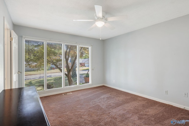carpeted empty room with visible vents, baseboards, and a ceiling fan