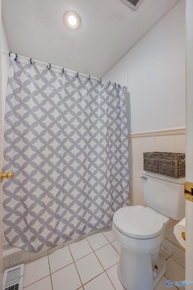 bathroom with tile patterned floors, a shower with curtain, a wainscoted wall, toilet, and visible vents