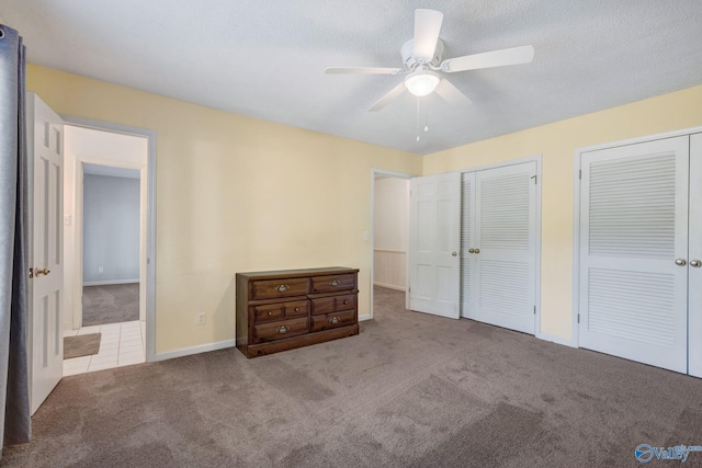 unfurnished bedroom featuring baseboards, two closets, a ceiling fan, a textured ceiling, and carpet flooring