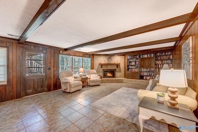 living area with a textured ceiling, wood walls, a brick fireplace, and beam ceiling