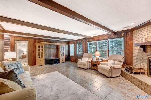 living area featuring a fireplace, wooden walls, a textured ceiling, visible vents, and beamed ceiling