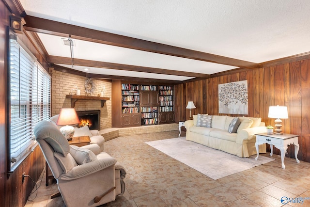 living room featuring wooden walls, a brick fireplace, a textured ceiling, and beam ceiling