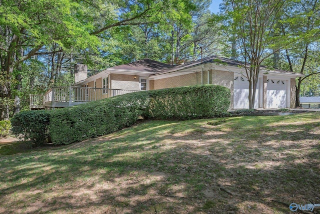 view of property exterior featuring a deck, a yard, a garage, a chimney, and brick siding