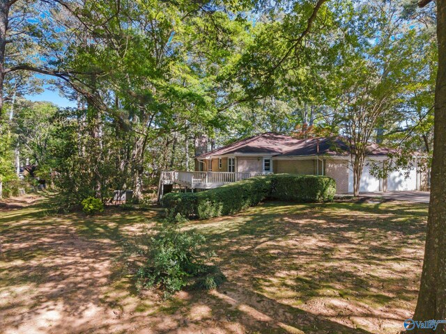 view of yard with driveway, a wooden deck, and an attached garage