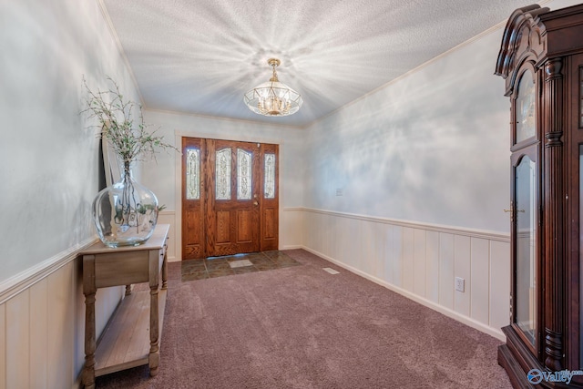 carpeted entryway with ornamental molding, an inviting chandelier, wainscoting, and a textured ceiling