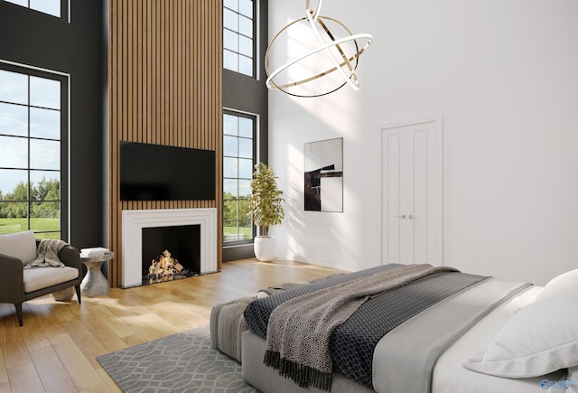 bedroom with a chandelier, a lit fireplace, wood finished floors, and a towering ceiling