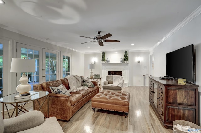 living room featuring light hardwood / wood-style flooring, ceiling fan, ornamental molding, a brick fireplace, and french doors