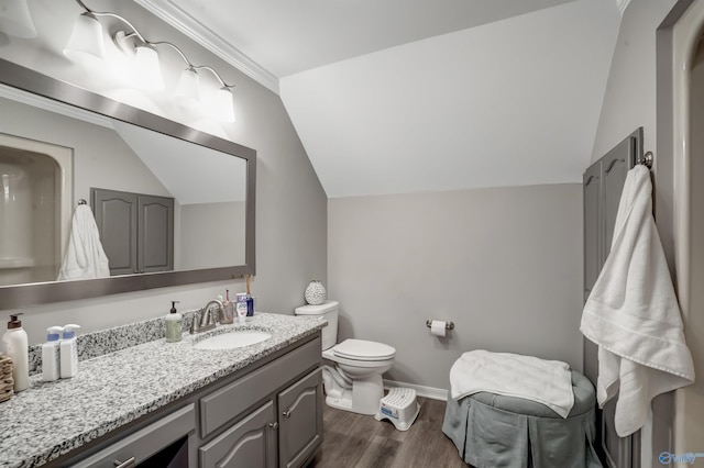 bathroom with wood-type flooring, lofted ceiling, vanity, toilet, and crown molding