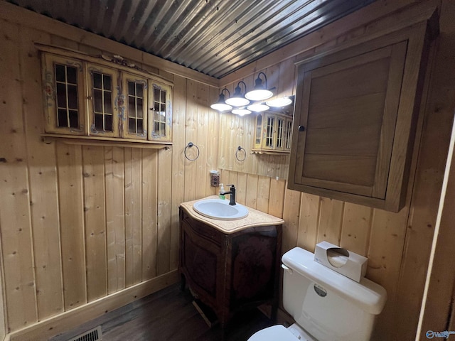 bathroom with toilet, wood finished floors, vanity, and wooden walls