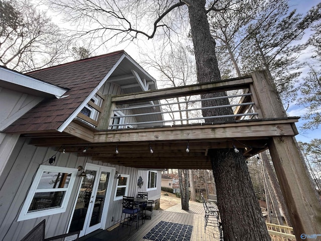 exterior space with roof with shingles, a deck, board and batten siding, and french doors