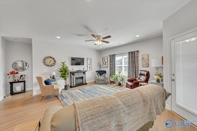 living room featuring light wood finished floors, baseboards, a glass covered fireplace, ceiling fan, and recessed lighting