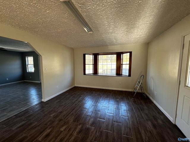 empty room featuring a healthy amount of sunlight, a textured ceiling, and dark wood-type flooring