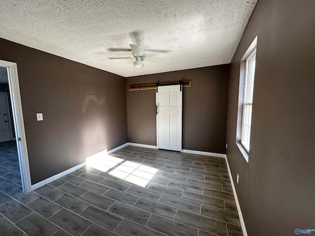 empty room with a barn door, a textured ceiling, ceiling fan, and tile patterned flooring