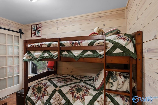 bedroom featuring hardwood / wood-style floors, wood walls, and a barn door