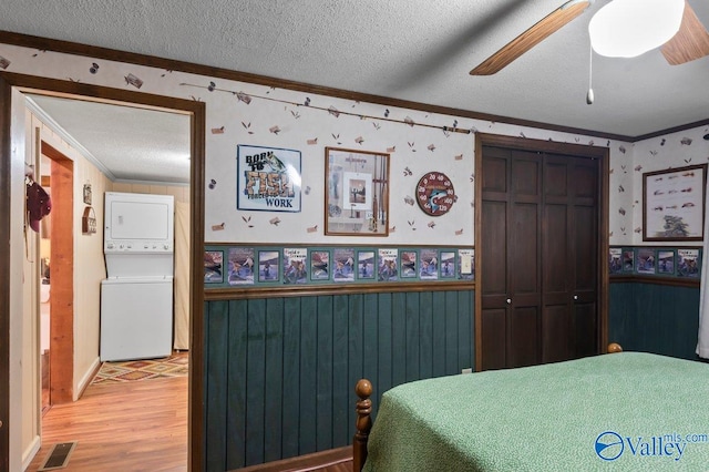 bedroom with hardwood / wood-style floors, a textured ceiling, ceiling fan, and stacked washer and clothes dryer