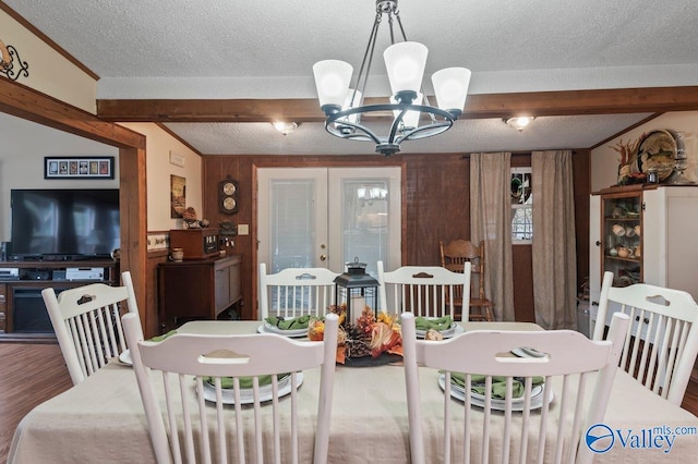 dining space with french doors, a textured ceiling, wood-type flooring, an inviting chandelier, and beamed ceiling