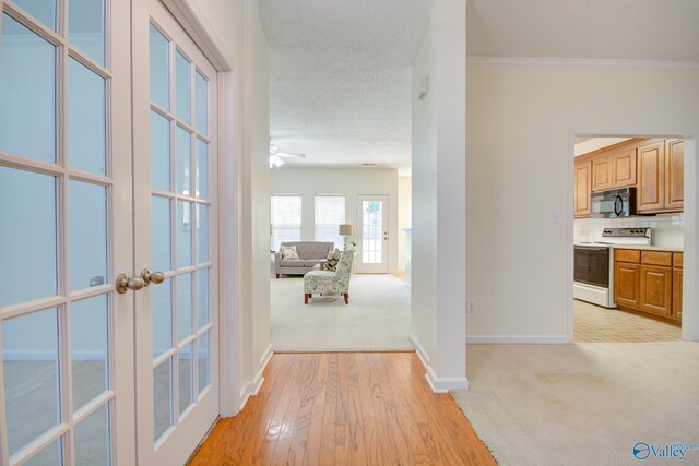 corridor featuring french doors, light wood-type flooring, and crown molding