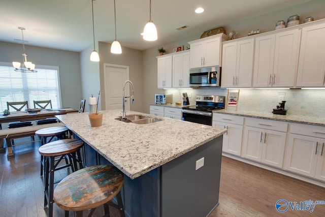 kitchen with white cabinetry, appliances with stainless steel finishes, hanging light fixtures, hardwood / wood-style floors, and an island with sink