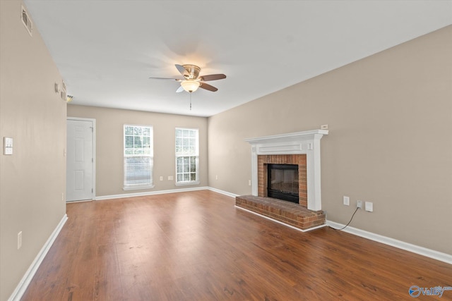 unfurnished living room with a brick fireplace, ceiling fan, visible vents, and wood finished floors