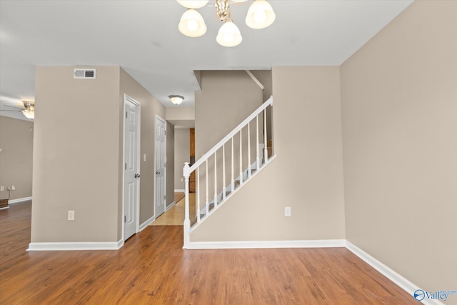 foyer entrance featuring baseboards, visible vents, stairway, wood finished floors, and ceiling fan with notable chandelier