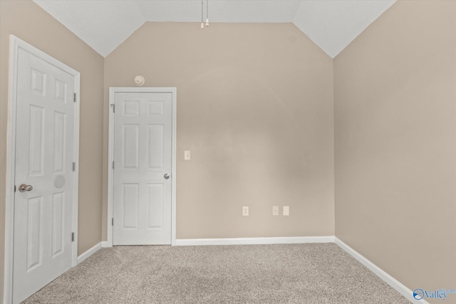 carpeted spare room featuring baseboards and vaulted ceiling