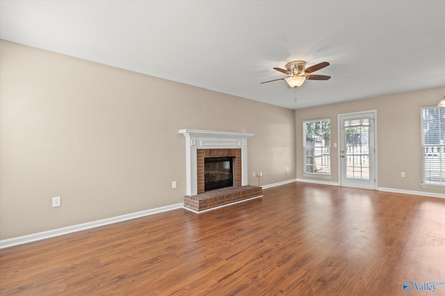 unfurnished living room featuring ceiling fan, a brick fireplace, wood finished floors, and baseboards