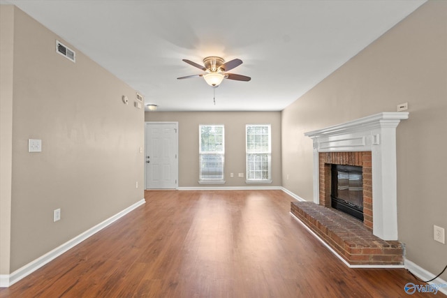 unfurnished living room featuring visible vents, baseboards, a ceiling fan, wood finished floors, and a brick fireplace