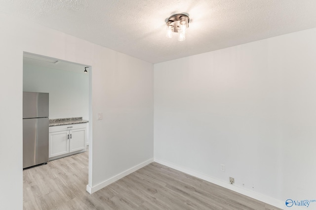 spare room featuring baseboards, a textured ceiling, and light wood-style floors