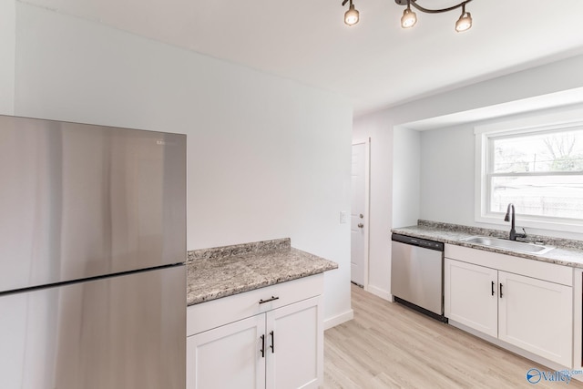 kitchen with a sink, white cabinetry, light wood-style flooring, baseboards, and appliances with stainless steel finishes