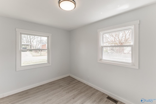 empty room with light wood-style flooring, visible vents, and baseboards